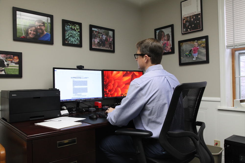 Trent Harris working in his office with photos on the wall of his family, children, and dog